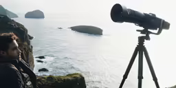 the man stands in front of a tripod holding a camera