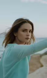 a woman is standing on the beach with her arm extended