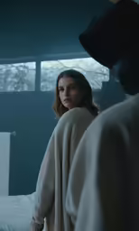 woman in cream top looking over bed with large window