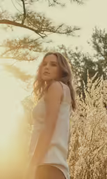 a woman stands in the forest as the sun sets