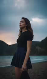 a woman wearing a skirt stands on the beach as the sun sets
