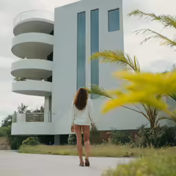 a woman walking along a sidewalk next to a building