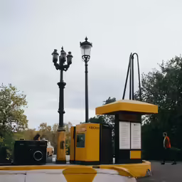 a yellow public restroom with light poles next to trees