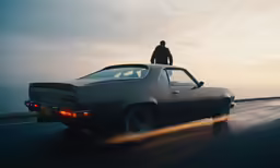 man standing on the hood of a car on a highway