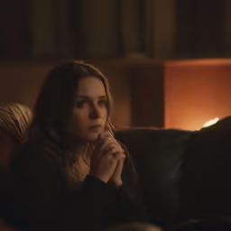 a young girl sits on a couch with her hands together