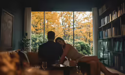 a man and woman sitting on a couch in a room filled with books
