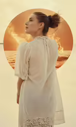 a woman standing by the ocean looking into a circle