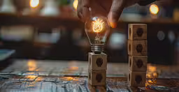 a person that is touching a lightbulb,a light bulb is shining in between two wooden blocks