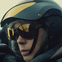 a man in a helmet and sunglasses looks off to the side
