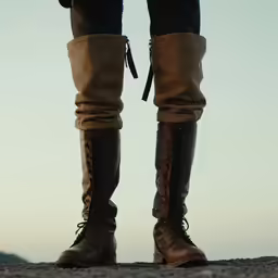 a person in high boots stands on a rock