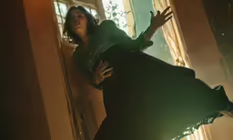 a woman in a green dress is leaning against a wall
