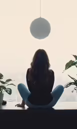 woman sitting with head tilted in meditation position with hanging plant in window