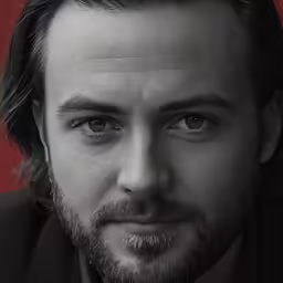 a portrait of a man with his hair in a low ponytail and wearing a black suit
