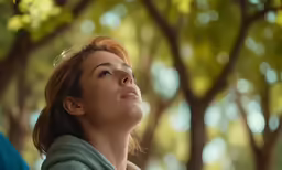 the woman looks up into the tree - lined sky