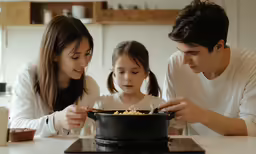 the woman and man are sitting next to the girl as they cook food in the skillet
