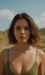 woman wearing bikini top standing in grass with hills behind her