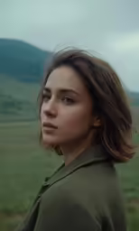 a beautiful woman standing in front of a lush green hillside
