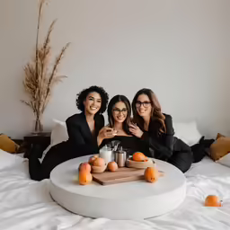 three women in black outfits pose for the camera on a bed