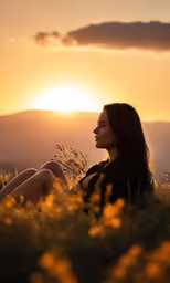 the woman is sitting in the grass watching the sun set