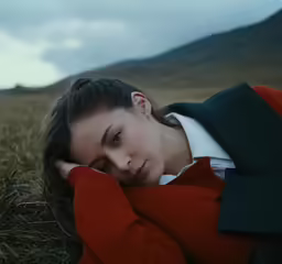 a woman is laying in a grassy field and she is wearing a jacket