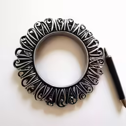 a pen sits next to an ornately designed metal ring with filigrees and swirl scrolls