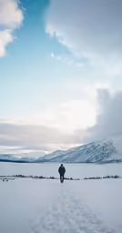 a person walking in the snow by mountains