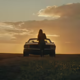 a woman sitting on the back of a car in a field at sunset