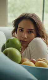 a woman sitting on a couch with a large bowl of apples