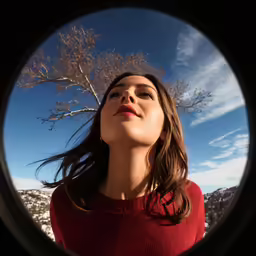 woman looking up into the sky from below with the camera pointed forward