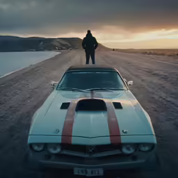 a man stands on top of an antique muscle car, with red and white stripes