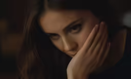 a woman is staring into the distance and holds her hands on her face