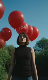 a woman in a black top holding onto red balloons