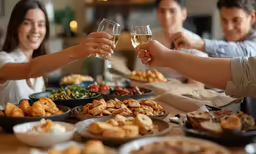 people toast with white wine while sitting around a table full of food