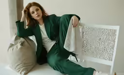 the woman sits on a bench and poses with her hand on her head