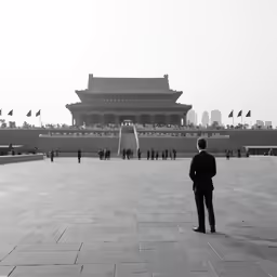 an asian man in a suit is facing a building with flags