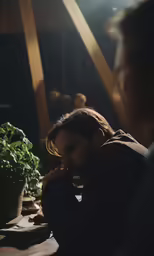 two people sitting at a table with a potted plant