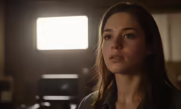 a woman looks into the distance in front of a bright window