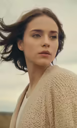 a woman with wind blown hair and an open knit sweater