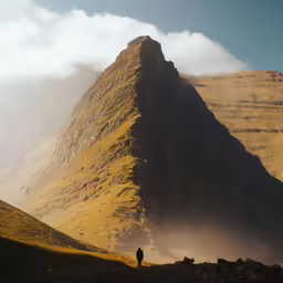 person standing on a rock - strewn mountain peak beneath a bright cloud filled sky