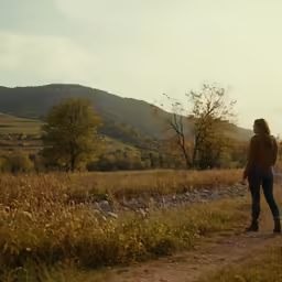 a woman standing in the grass and looking down a trail