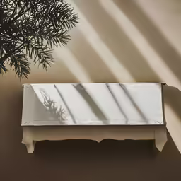a white bench with a shadow on the wall
