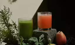 a green smoothie with a glass of juice next to it