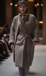 a woman wearing a gray coat is standing on the runway