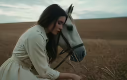 woman kneeling down while petting a horse in an open field