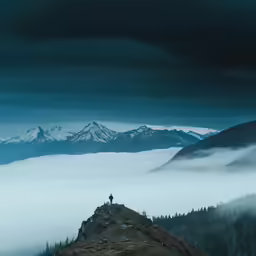 man standing on top of mountain with clouds and fog