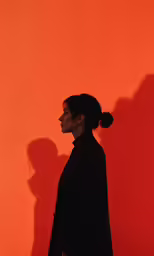 a silhouette of a woman standing against an orange wall