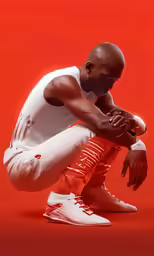 a man crouching and wearing sneakers with red background