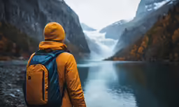 someone wearing a yellow and blue jacket and a backpack standing on the edge of a lake