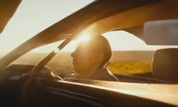 the woman sits in her car at sundown