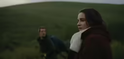 a young man and woman in coats look off into the distance